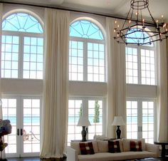 a living room filled with lots of windows next to a chandelier and two couches