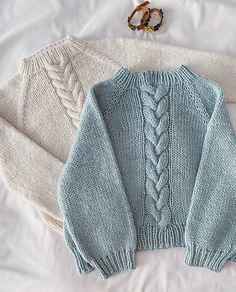 two knitted sweaters laying next to each other on a white sheet with beads