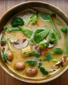 a bowl of soup with broccoli, mushrooms and other vegetables in it on a wooden table