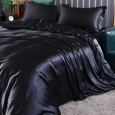 a bed with black sheets and pillows on top of carpeted floor next to a green chair