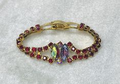 A 50's colorful bracelet of red rhinestones in a festoon design, faced with two aurora borealis baguette stones, one faceted and the other pressed in a leaf pattern. It closes with a hinged clip,  It measures 7" long and 3/8" wide. The face is 3/4". Excellent condition. Catalog # 8844 Vintage Red Bracelets For Party, Red Jeweled Bracelet For Party, Formal Red Crystal Bracelets, Red Vintage Party Bracelets, Red Jubilee Bracelets For Parties, Red Jubilee Bracelet For Party, Red Crystal Rhinestone Bracelet For Party, Red Crystal Bracelet With Rhinestones For Party, Red Rhinestone Crystal Bracelet For Party