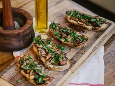 bread with mushrooms and greens on a cutting board next to a bottle of olive oil