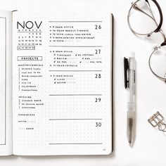 an open notebook on top of a table next to glasses and pen, eyeglasses