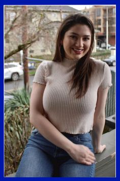 a woman is sitting on a ledge with her hands in her pockets and smiling at the camera