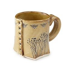 a ceramic mug with bees and flowers on it's side, sitting in front of a white background