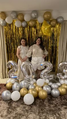 two women standing next to each other in front of balloons and the number twenty five