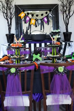 the table is set for halloween dinner with purple and green decorations, black tablescloths, and white chairs