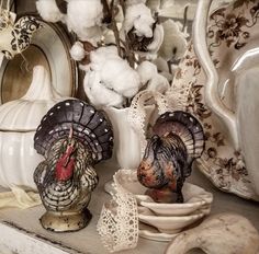 two turkey figurines sitting on top of a table next to plates and bowls