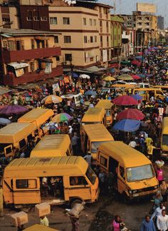 a large group of people standing around yellow buses in the middle of a busy street