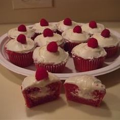 cupcakes with white frosting and raspberries are arranged on a plate