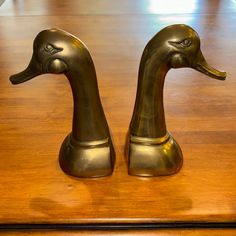 two brass ducks sitting on top of a wooden table