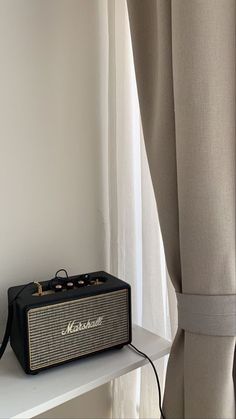 an old radio sitting on top of a white shelf next to a window with curtains