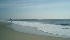 a man standing on top of a beach next to the ocean holding a fishing pole