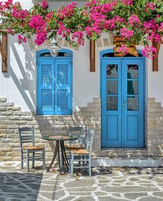 two blue doors are open on the side of a building with flowers growing over it