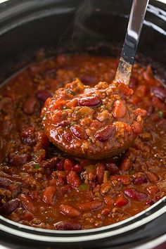 a slow cooker filled with chili and meat in the crock pot is being held by a ladle