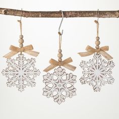 three snowflakes hanging from a tree branch with ribbon and bows attached to them