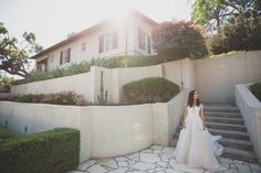 a woman standing in front of a white building with stairs and bushes on the side