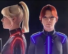 two women in futuristic outfits with neon lights on their shoulders and back, facing each other