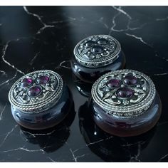 three black and silver boxes sitting on top of a marble table with red stones in the middle