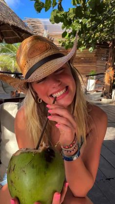 a woman wearing a straw hat holding a green coconut