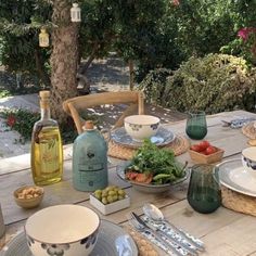 the table is set with plates, bowls and cups on it for an outdoor meal