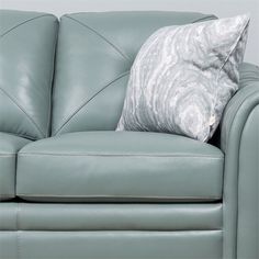 a light green leather couch with a silver pillow on it's arm and back