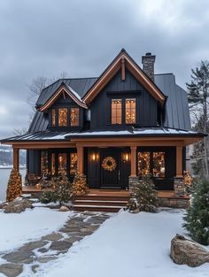 a black and brown house with christmas lights on the front porch, trees and rocks