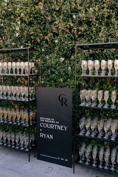 there are many wine glasses on display in front of a wall with greenery behind it