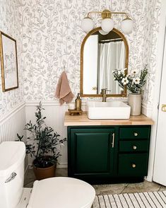 a white toilet sitting next to a bathroom sink under a mirror on top of a wooden counter