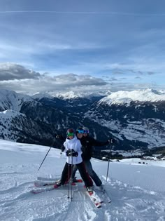 two people on skis posing for a photo in the snow with mountains behind them