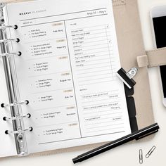 an open planner sitting on top of a desk next to a cell phone and pen