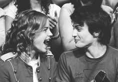 black and white photograph of two young men laughing at each other in front of a crowd