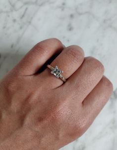 a woman's hand with a diamond ring on top of her left hand and marble background