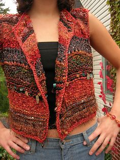 a woman standing in front of a house wearing a red and black knitted vest