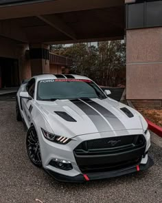 the front end of a white and black mustang parked in a parking lot next to a building