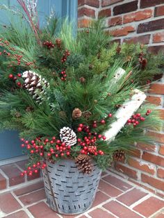 a basket filled with pine cones and red berries on the front door sill next to a brick wall