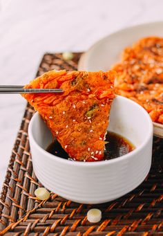 a person dipping some food into a bowl with chopsticks on the table next to it