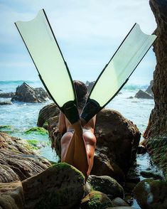 a woman sitting on some rocks with her legs crossed and two large surfboards sticking out of her head