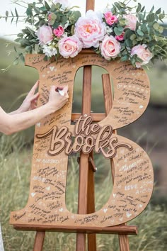 a wooden sign with writing on it and flowers in the top right corner is being held up by a woman