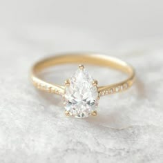 a yellow gold engagement ring with a pear shaped diamond in the center and side stones