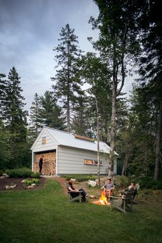 people sitting around a campfire in front of a small building with a shed on the side