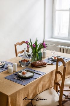 a table set for two with flowers in the vase and bread on the plate next to it