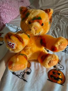 a yellow teddy bear sitting on top of a white bed covered in halloween themed sheets