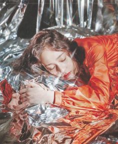 a woman in an orange jacket is laying on tin foil and looking at her cell phone