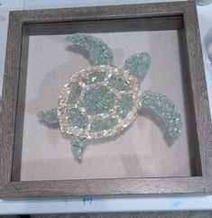 a sea turtle made out of glass and beads in a shadow box on a table