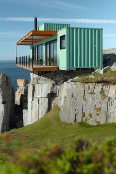 a green shipping container sitting on top of a cliff next to the ocean