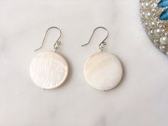 These are a pair of over-sized sea shell dangle earrings featuring 25 mm diameter cream to white colour natural sea shell buttons, and handmade sterling silver ear wire.  The sea shell buttons are each different and displays beautiful pattern and sheen, and are very eye catching  due to their size. The earring design is simple and elegant, and can be dressed up or down, to pair with different outfits, and to add some ocean's healing to your life. With the warmer months ahead, these earrings will definitely come in handy. Sea Shells stimulate intuition, sensitivity, imagination and adaptability. They have the natural ability to disperse negative energy. They also provides gentle but thorough healing energy which works with the healer to cleanse, balance and harmonize chakras and the aura. M White Mother Of Pearl Earrings, White Shell Earrings With Pearl Drop, White Shell-shaped Pearl Drop Earrings, White Shell Shaped Pearl Drop Earrings, White Shell Earrings For Pierced Ears, White Round Mother Of Pearl Earrings, White Mother Of Pearl Round Earrings, Adjustable White Mother Of Pearl Earrings, Adjustable Round Mother Of Pearl Earrings