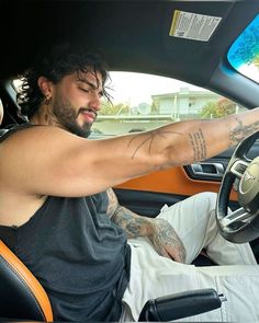 a man sitting in the driver's seat of a car with tattoos on his arm