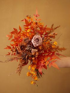 a woman holding a bouquet of flowers and leaves in front of a brown wall with an orange background