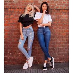 two women standing next to each other near a brick wall